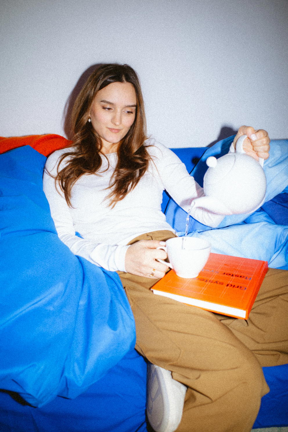 Tanja - Woman pouring tea on couch with orange book